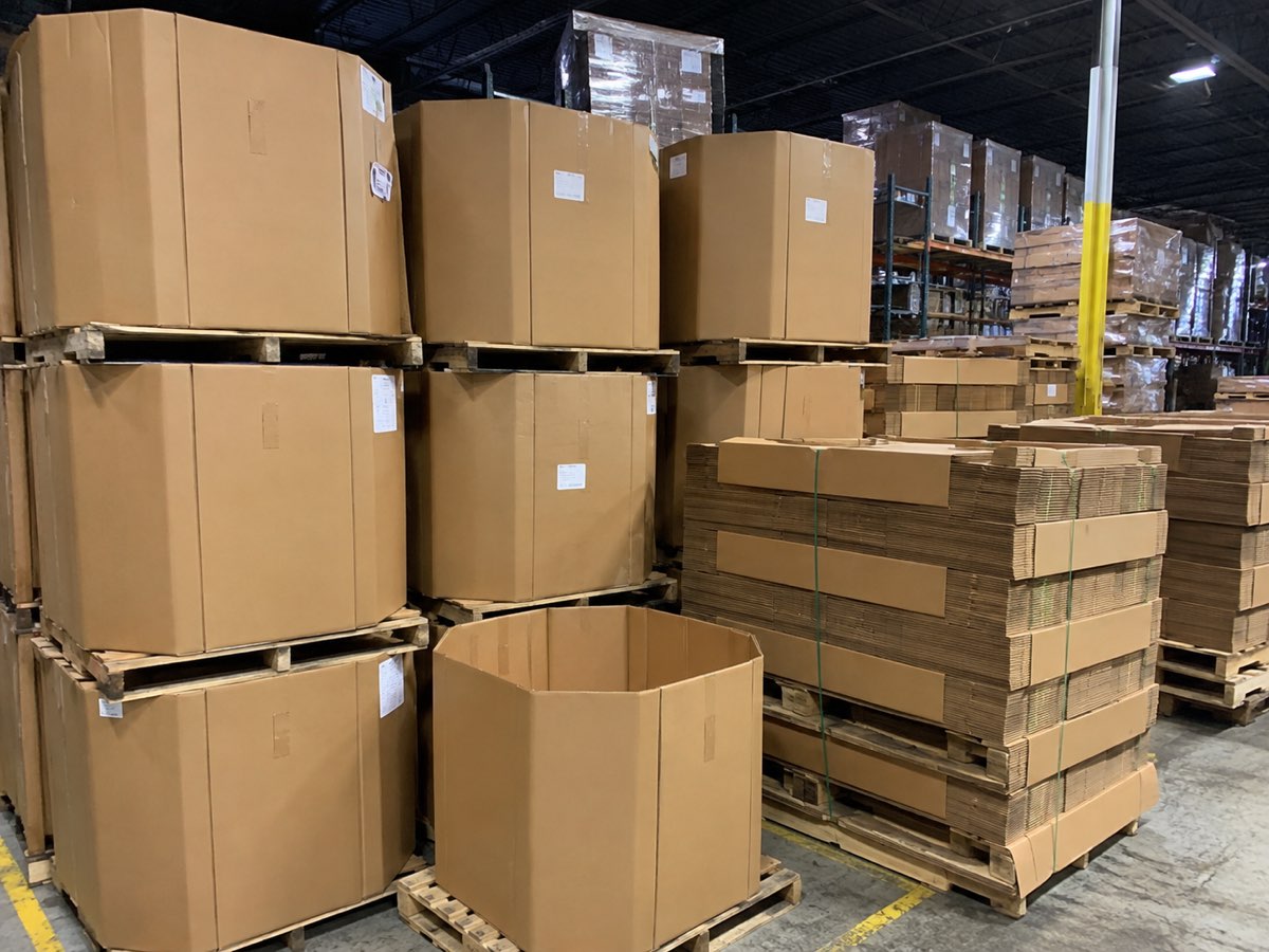 Bulk bins stacked two high on pallets down a warehouse aisle, with banded knocked-down bundles alongside