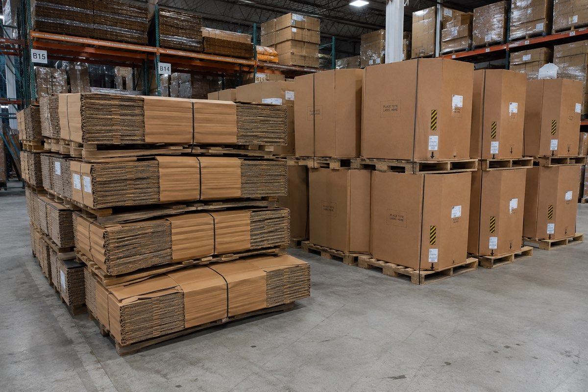 Flat banded bundles of knocked-down boxes on the left and assembled bulk bins on pallets on the right